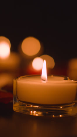 Vertical-Video-Close-Up-Of-Romantic-Lit-Red-And-White-Candles-Burning-On-Black-Background-With-Bokeh-Lighting-5